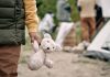 Child holding teddy bear near people and tent outside.