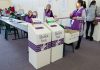 Election polling station with ballot boxes and officials.