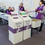 Election polling station with ballot boxes and officials.