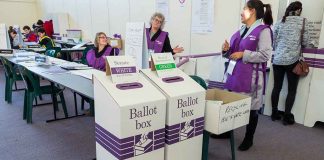 Election polling station with ballot boxes and officials.