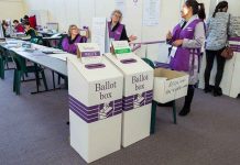 Election polling station with ballot boxes and officials.