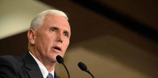 Man in suit speaking at podium with two microphones.