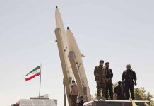 Military personnel beside missiles and Iranian flag.