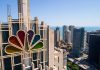 Colorful peacock logo on high-rise building overlooking city.