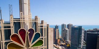 Colorful peacock logo on high-rise building overlooking city.