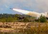 Military tank firing a missile in forest area.