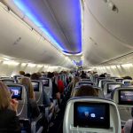 Airplane cabin with passengers and in-flight entertainment screens.