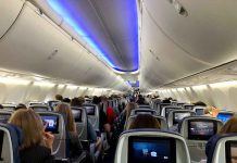 Airplane cabin with passengers and in-flight entertainment screens.