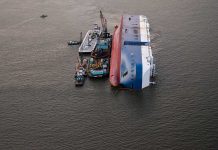 Capsized ship with cranes and tugboats around it.