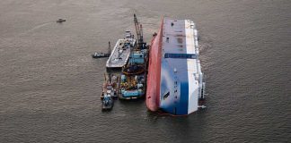 Capsized ship with cranes and tugboats around it.