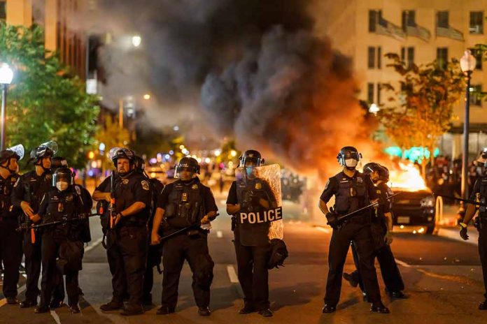 Police officers in riot gear near burning car.