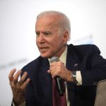 Man holding microphone and gesturing while speaking.