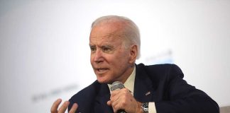 Man holding microphone and gesturing while speaking.