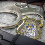 Handcuffs, officer badge, and firearm on textured surface.