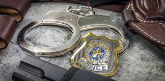 Handcuffs, officer badge, and firearm on textured surface.