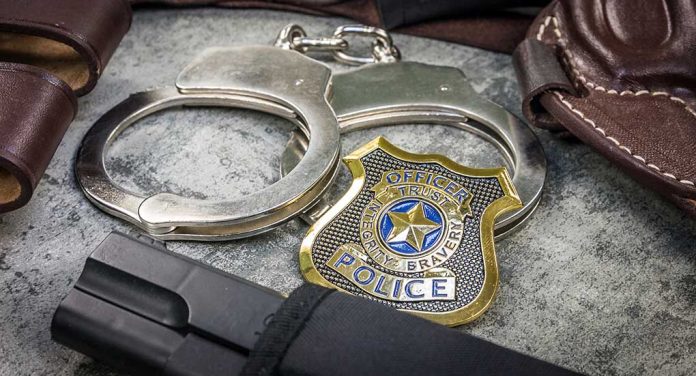 Handcuffs, officer badge, and firearm on textured surface.