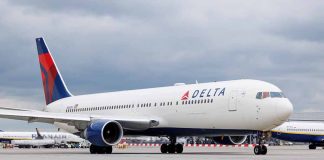 Delta Airlines airplane on airport runway, cloudy sky.