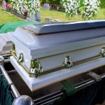 White coffin at a cemetery with flowers nearby.