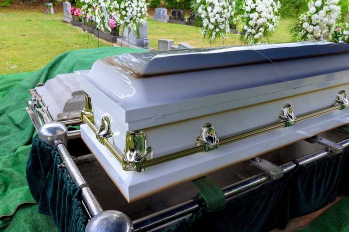 White coffin at a cemetery with flowers nearby.