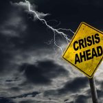 Yellow "Crisis Ahead" sign with stormy sky.