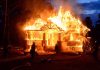 House engulfed in flames with firefighters present.