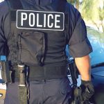 Police officer in uniform standing near a patrol car.