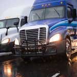 Two trucks driving on a wet road.