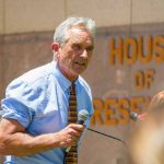 Man speaking into microphone outside government building.