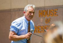 Man speaking into microphone outside government building.