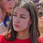 Woman in red shirt with serious expression, background blurry.