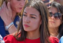 Woman in red shirt with serious expression, background blurry.