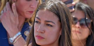 Woman in red shirt with serious expression, background blurry.