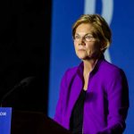 Woman in purple jacket speaking at podium.