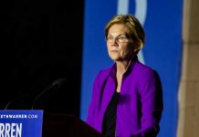 Woman in purple jacket speaking at podium.