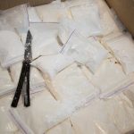 Bags of white powder with scissors in cardboard box.