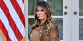 Woman in brown coat with American flag background.