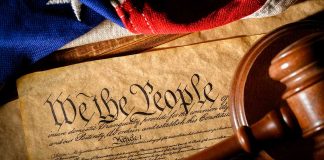 Gavel on U.S. Constitution with flag backdrop.