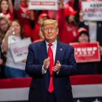 Man in suit clapping at rally with crowd.