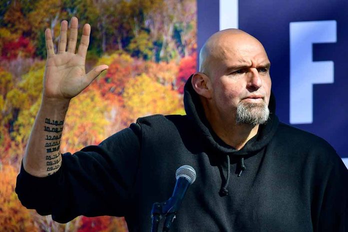 Man in black hoodie raising hand, speaking at microphone.