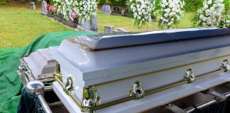 White coffin at a cemetery with flowers nearby.