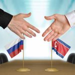 Two hands near flags of Russia and North Korea.