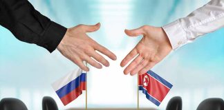 Two hands near flags of Russia and North Korea.