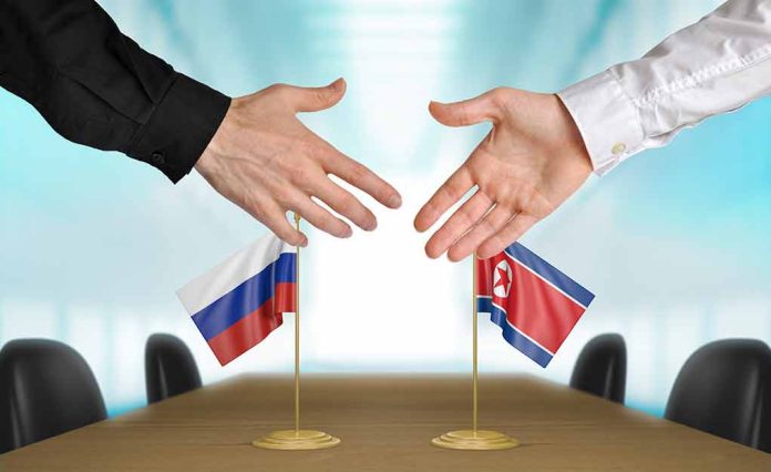 Two hands near flags of Russia and North Korea.