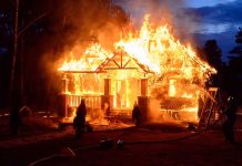 House engulfed in flames with firefighters present.