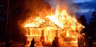 House engulfed in flames with firefighters present.