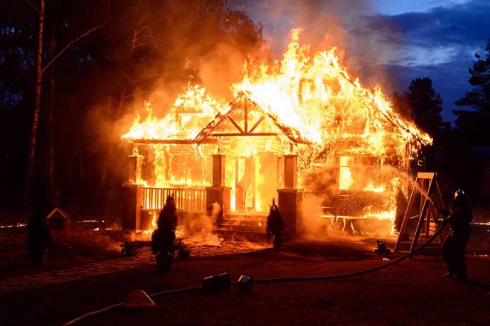 House engulfed in flames with firefighters present.