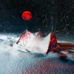 Red moon above snowy tent in blizzard night