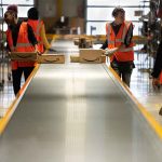 Workers in warehouse sorting packages on conveyor.