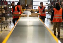 Workers in warehouse sorting packages on conveyor.