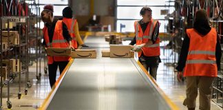 Workers in warehouse sorting packages on conveyor.